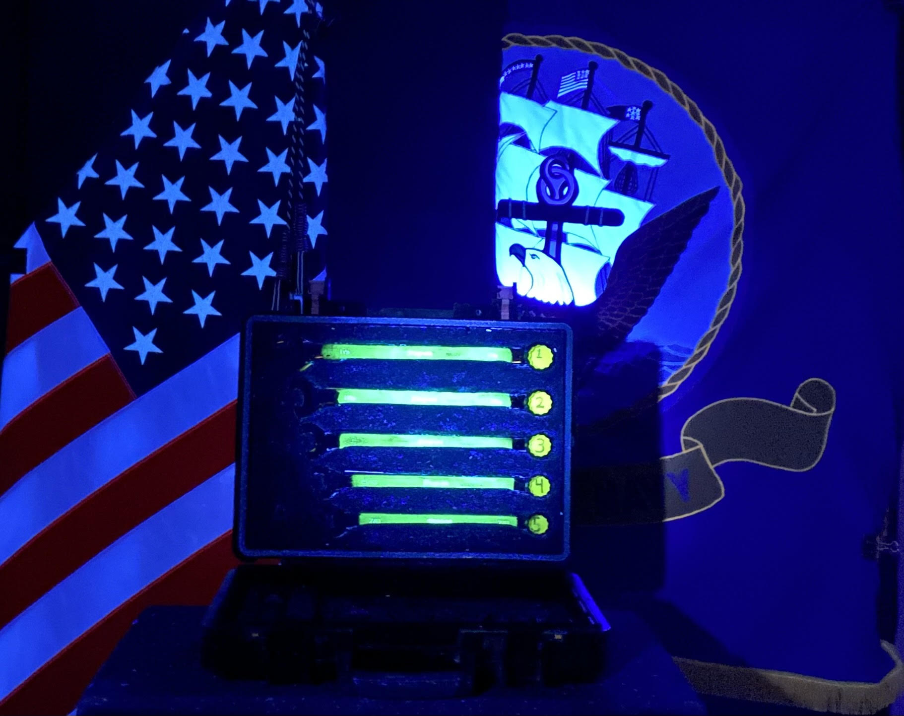 Glowing tools case under UV light with U.S. and U.S. Navy flags in the background